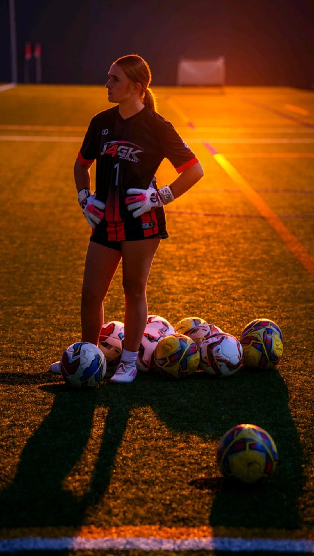 Female goalkeeper in Just4GK kit standing with soccer balls at golden hour