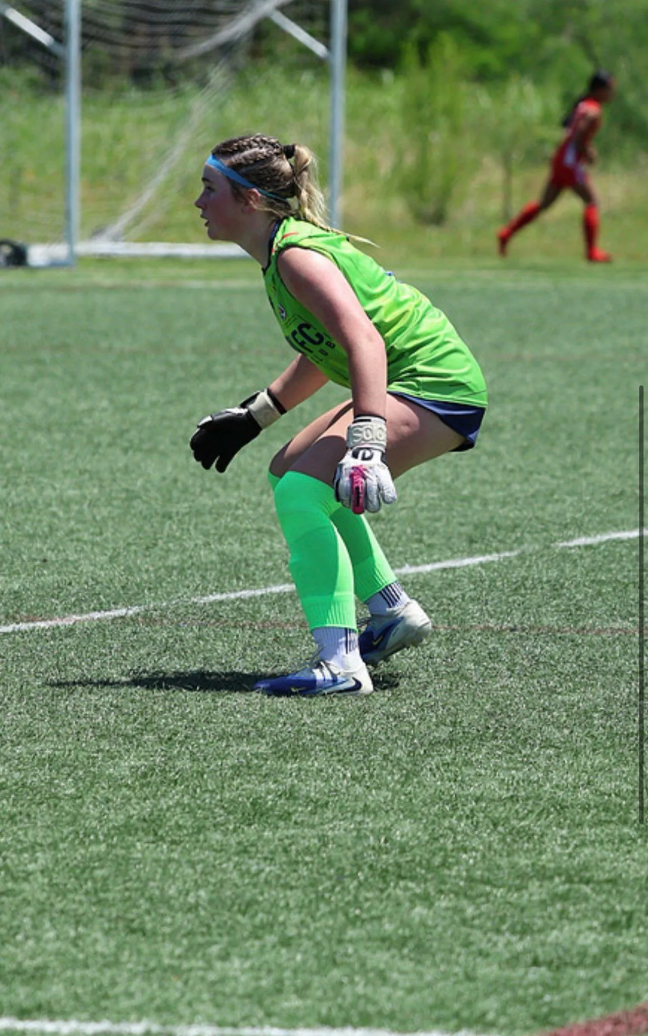Female goalkeeper in green holding a set position on a sunny field